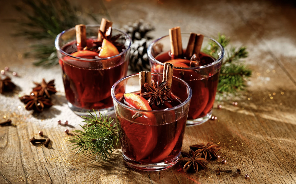 Mulling the Holiday Spirits Three glass mugs of mulled wine on a wooden table with pine needles and anise.